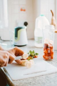 Preparing fresh smoothie with sliced banana and strawberries in kitchen setting.